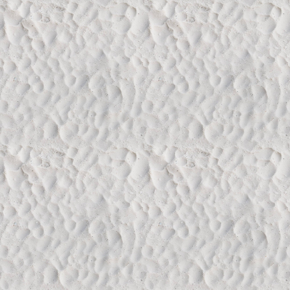 Close-up view of white sand with a pattern of small, uneven ridges and shallow depressions.